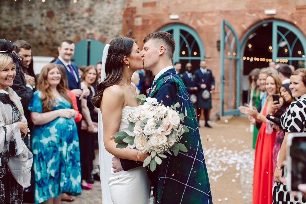 Wedding guests celebrate by throwing white flower petals in the air during an outdoor ceremony.