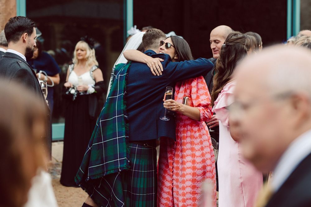 Wedding guests dance and celebrate together at a reception with people wearing plaid and coral colored attire.