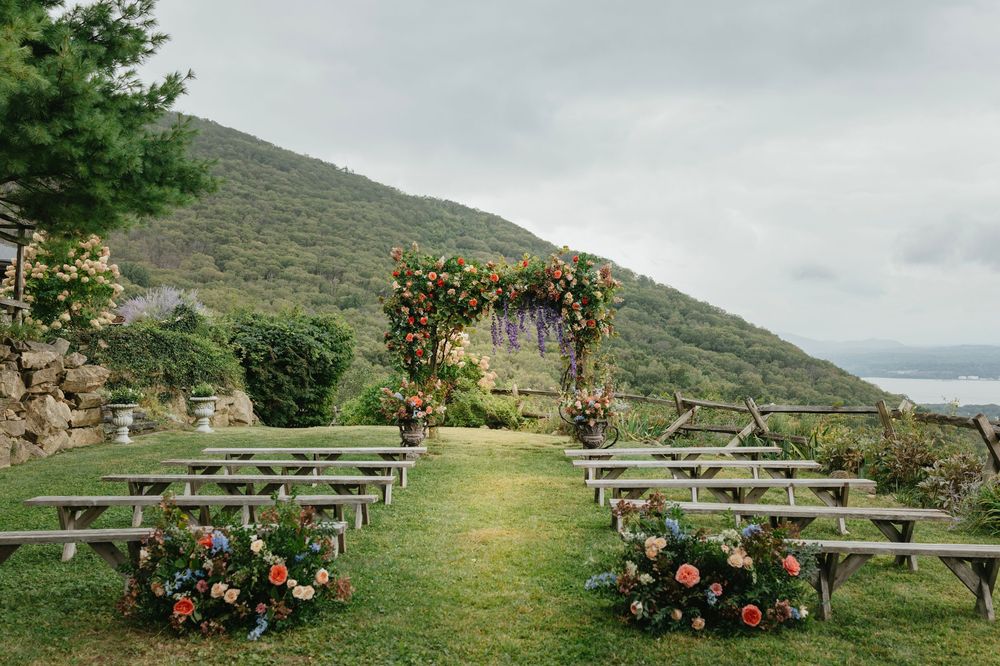 Rustic wooden benches arranged on a grassy hillside with mountain views and floral arrangements for an outdoor wedding.
