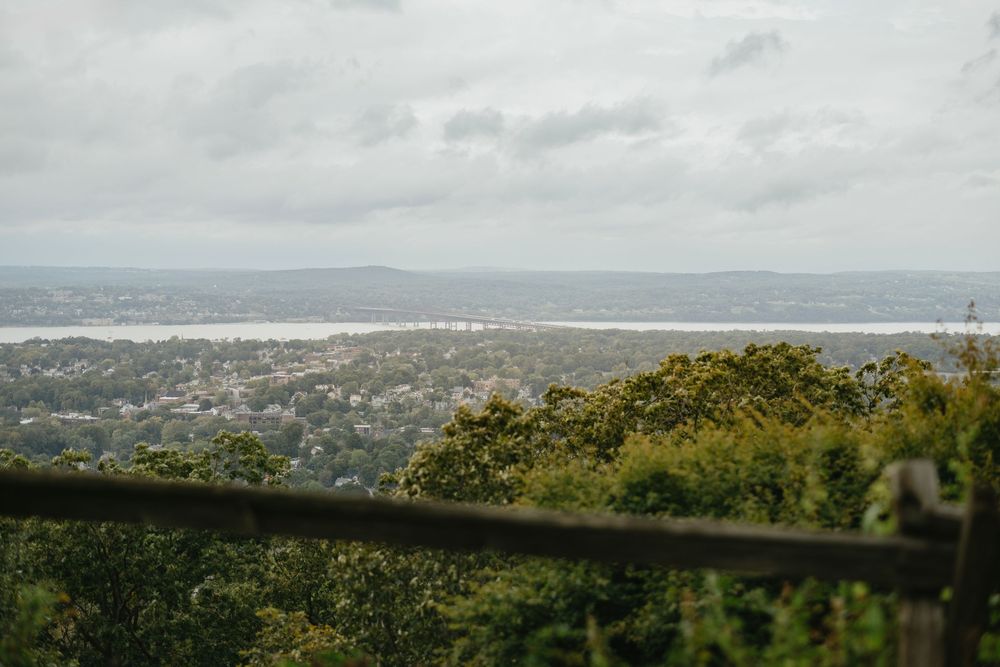 Panoramic view of a coastal city nestled between lush green hills and blue ocean waters under cloudy skies.