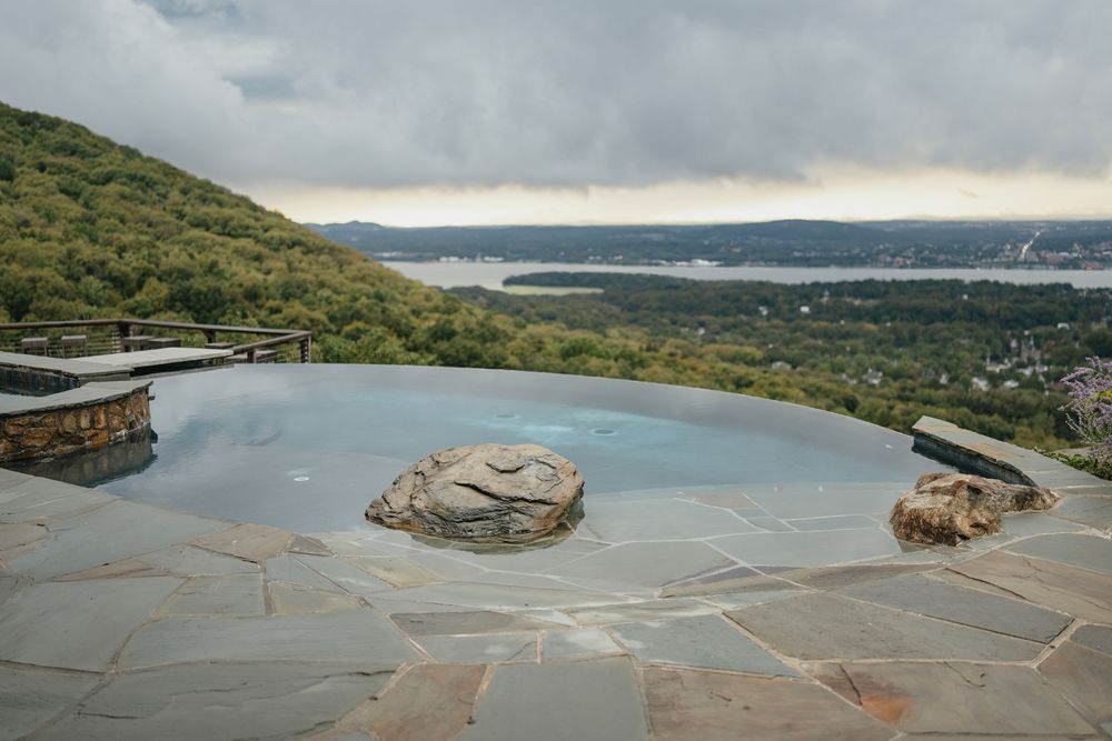 Aerial panoramic view of a scenic coastline with winding roads and lush green hills overlooking a tranquil bay.