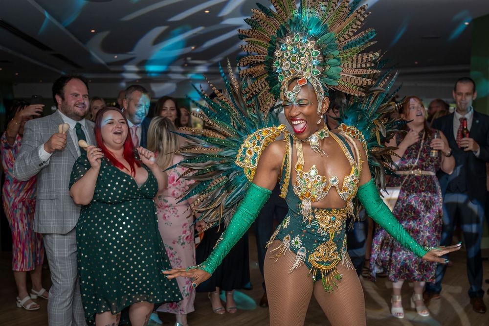 Carnival dancers in vibrant green costumes perform at an indoor celebration.