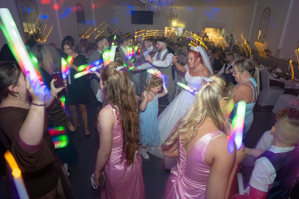 Wedding party dancing with glowing LED light sticks under colorful disco lights.