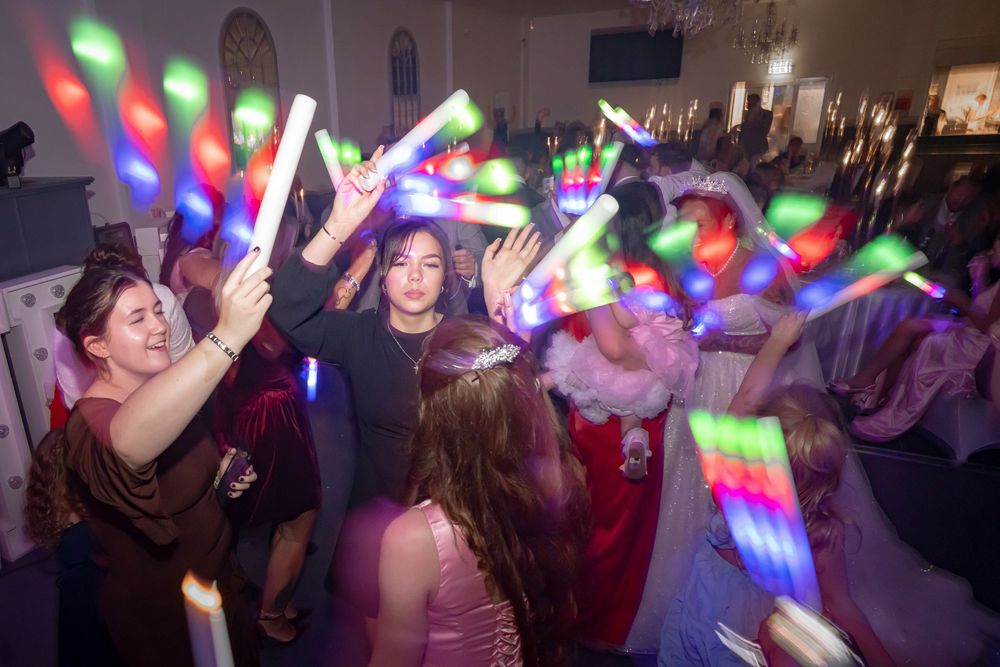 Guests waving colorful LED light sticks on a crowded dance floor at a wedding reception.