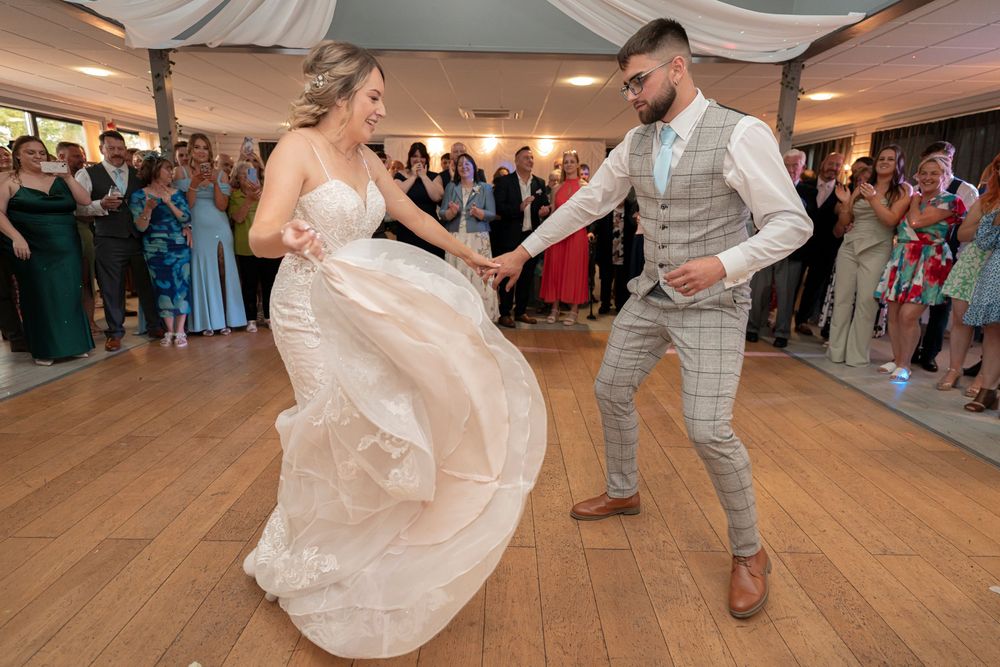 Wedding party members dancing and celebrating on a wooden dance floor with fabric decor overhead.