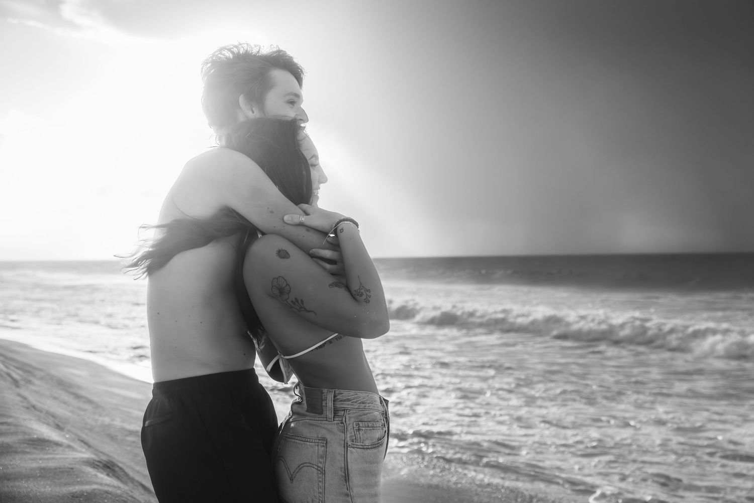 A romantic black and white photo series shows a couple embracing on a beach with ocean waves in the background.