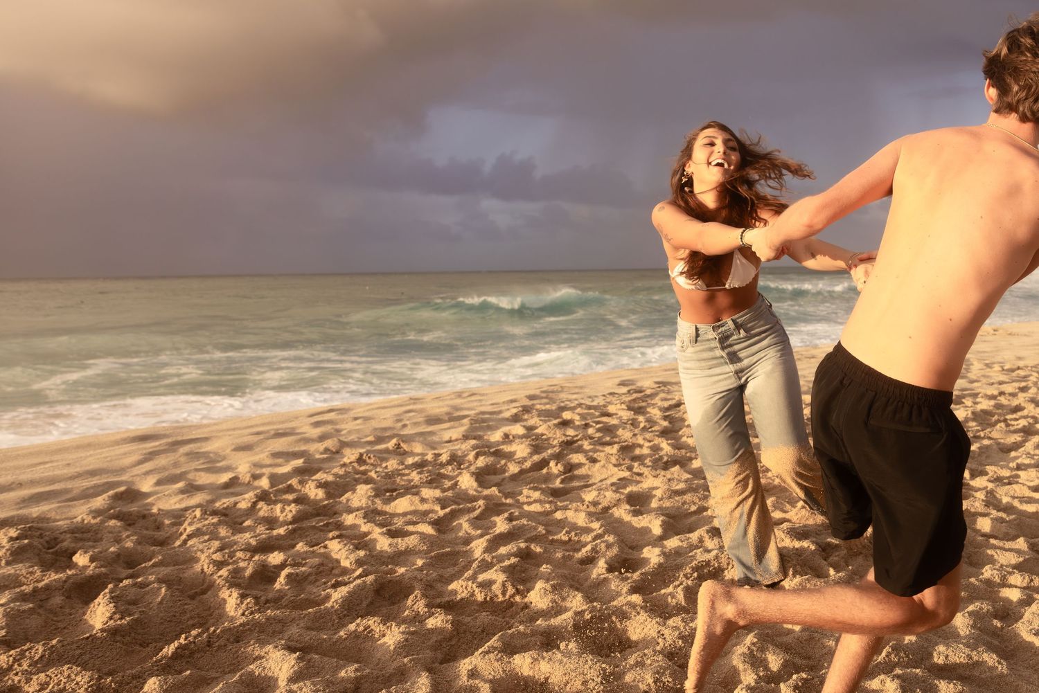 People enjoying a scenic beach photoshoot during golden hour with dramatic cloudy skies and crashing waves.