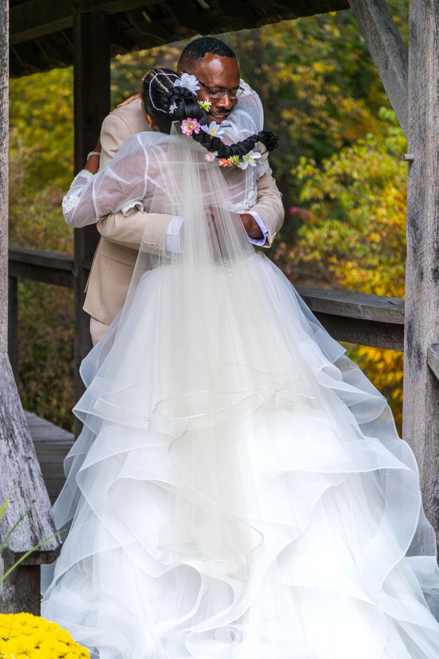 Groom helps bride in white gown rise from grass at outdoor wedding ceremony with colorful bouquet.