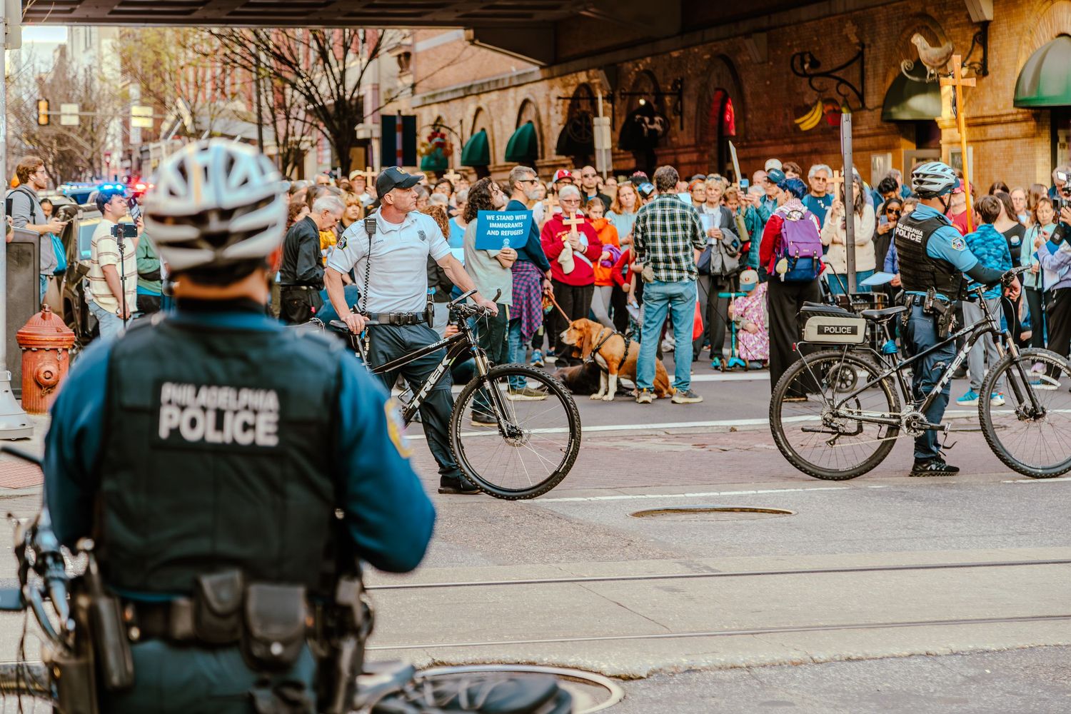 Large group of protesters marching through urban streets holding signs and banners during a daytime rally.