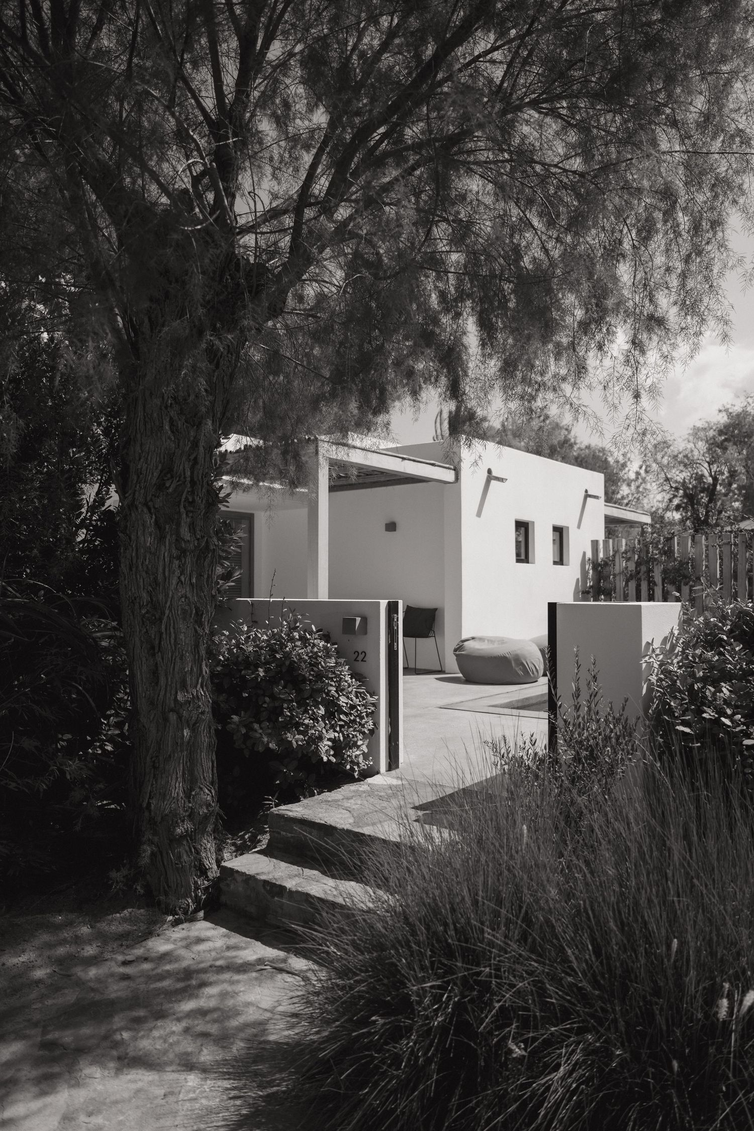 Black and white architectural photo series showing a modern minimalist house with white walls nestled among trees.