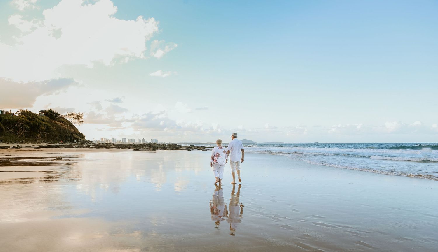 Silhouettes of people walking along a scenic beach shoreline at sunset with waves lapping at their feet.