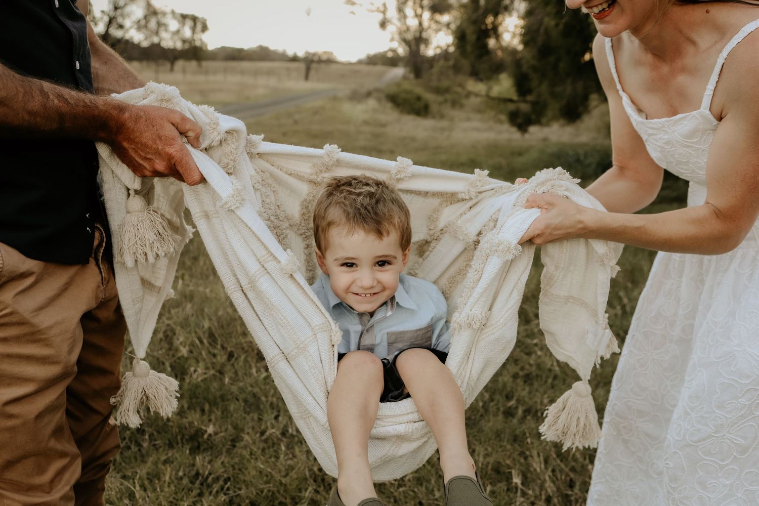 A group gathers outdoors in a field holding white fabric while playing a parachute game at sunset.