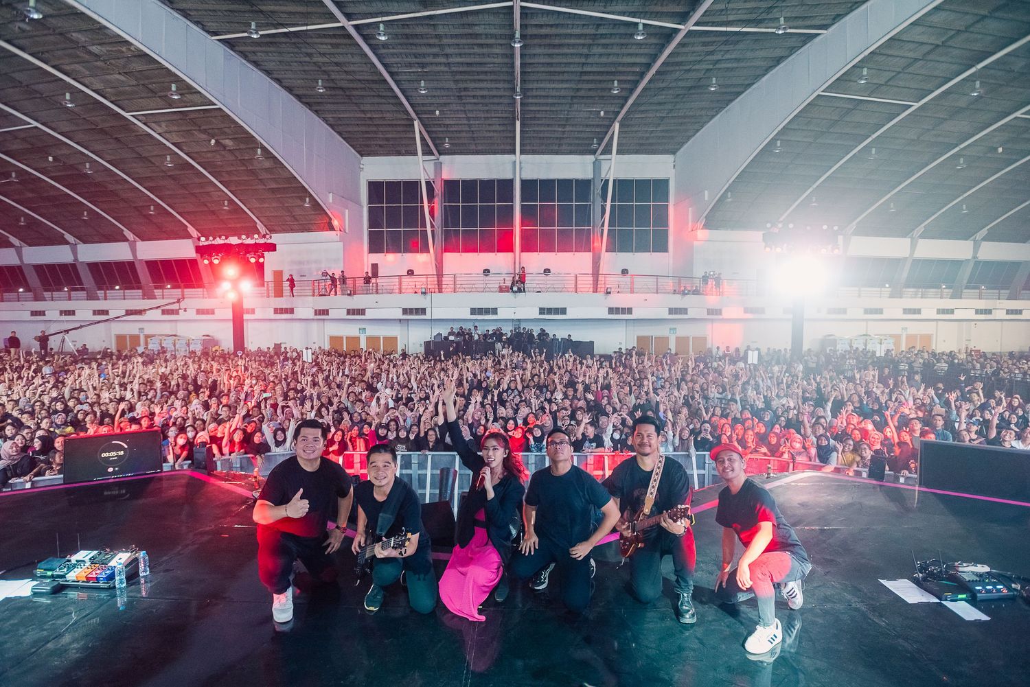 Band poses with large crowd in packed indoor venue during energetic live concert event.