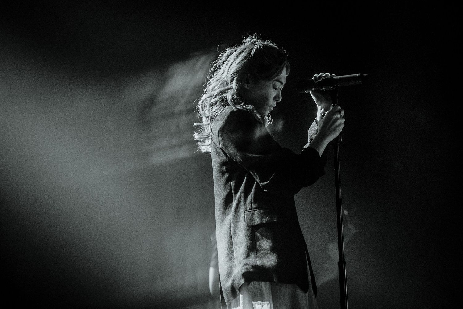 Black and white photo of a female singer performing on stage with a microphone in dramatic lighting.