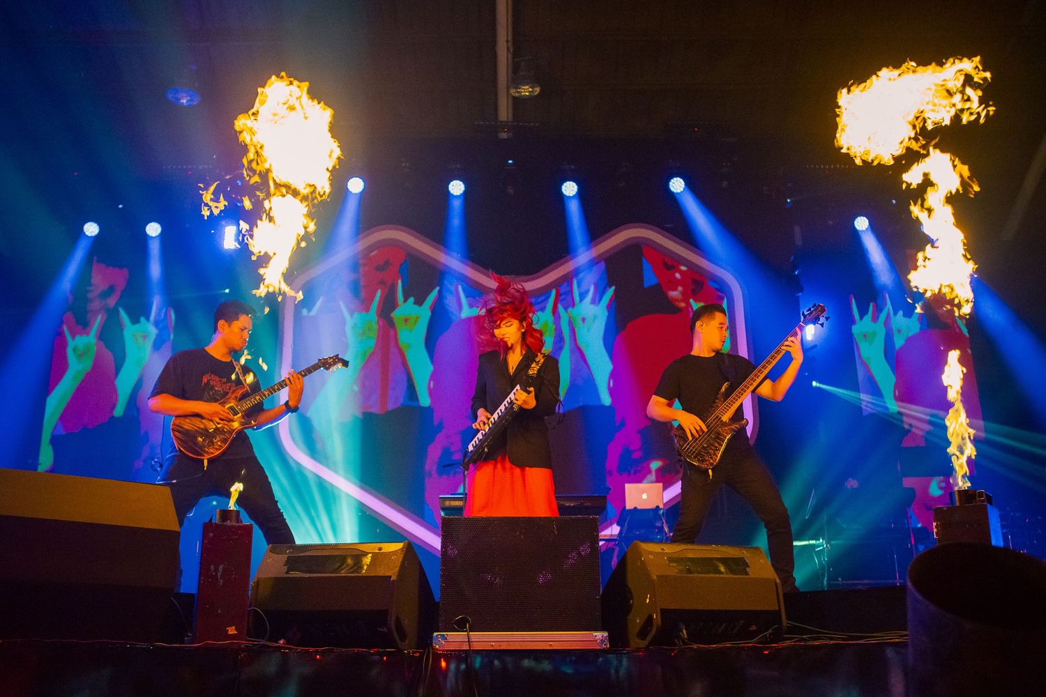 Rock band performing on stage with dramatic fire effects and colorful blue and purple lighting.