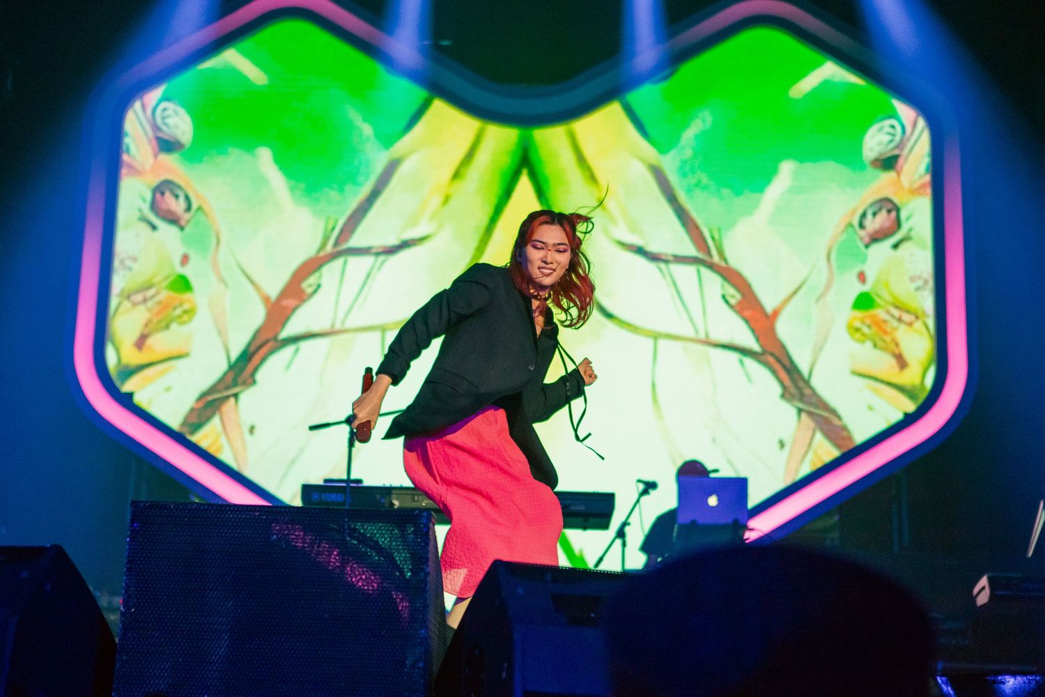 Energetic performer dancing on stage with vibrant green LED backdrop and pink pants at a live concert.
