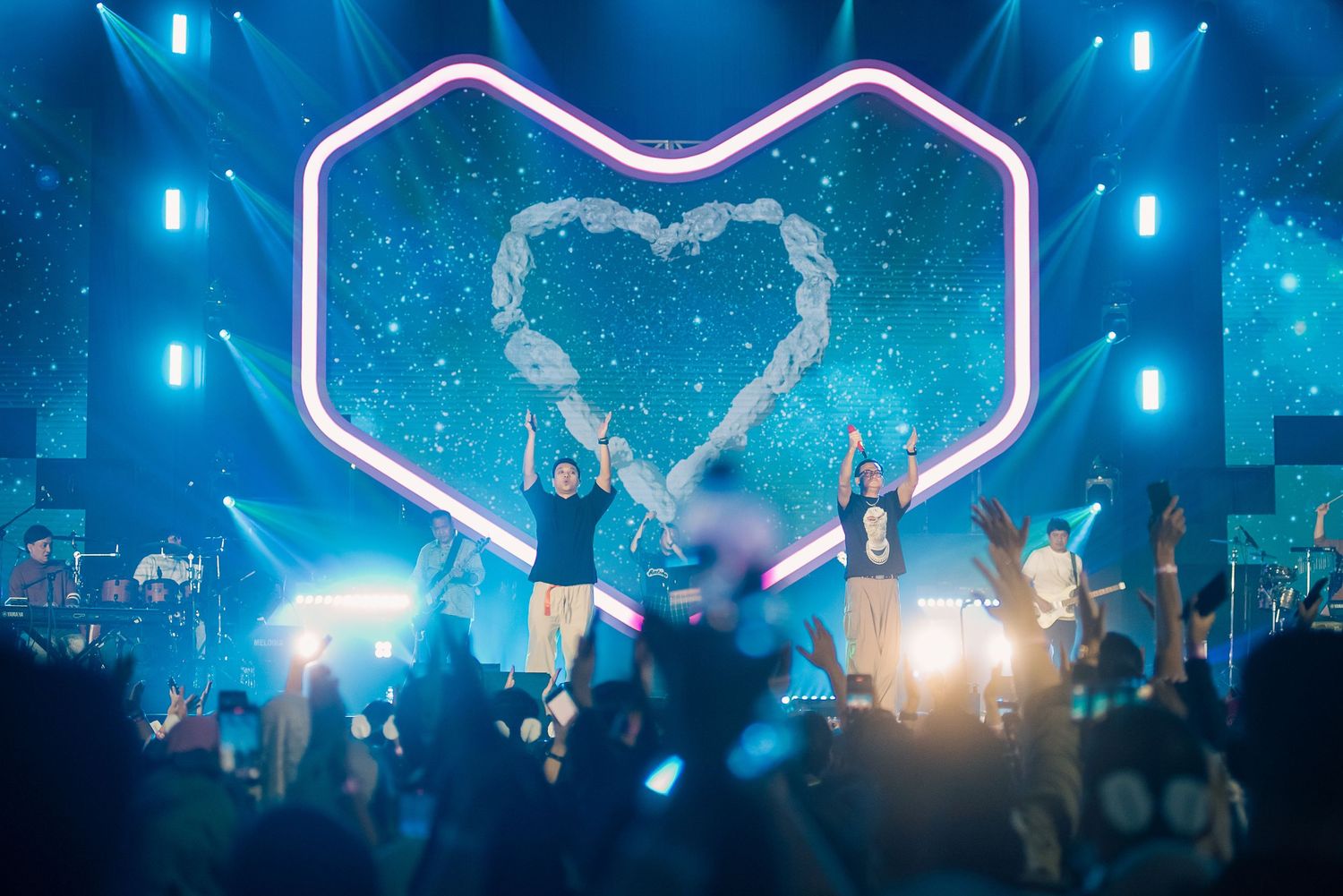 Performers on stage with heart-shaped backdrop and blue lights at a live concert event.