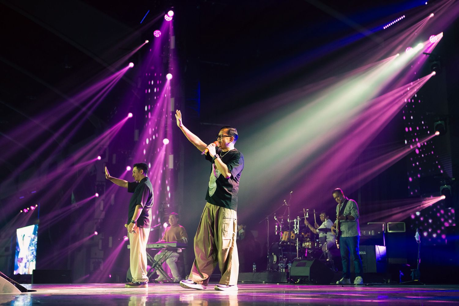 Performers on stage with purple and white spotlights during a live concert event.
