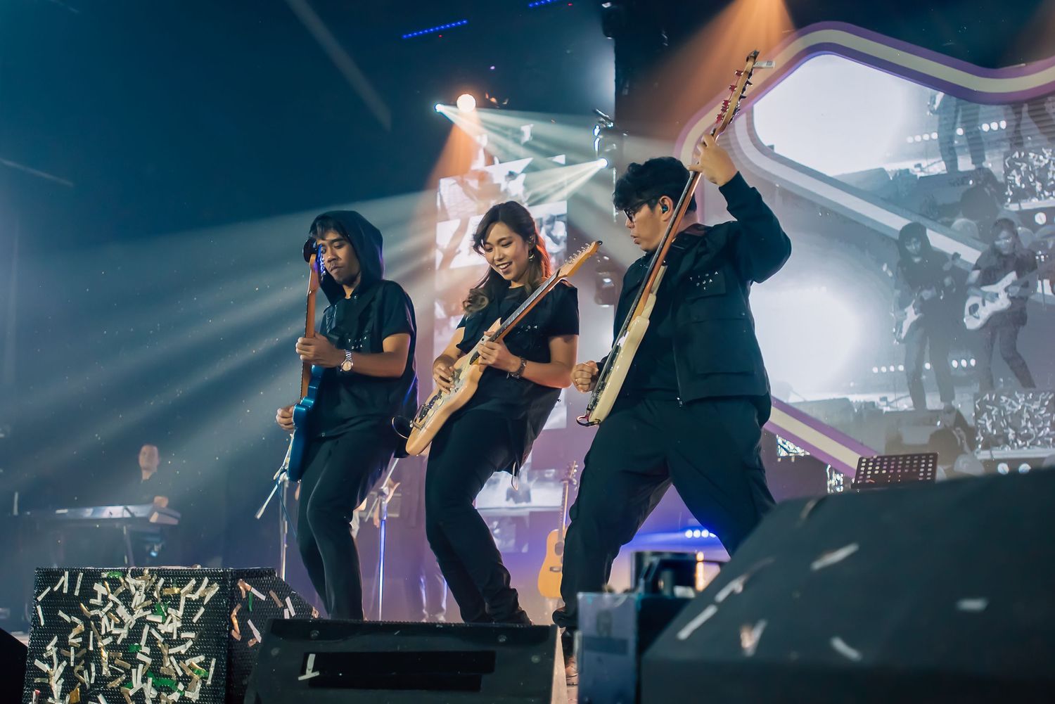 Three musicians performing energetically on stage with electric guitars under bright concert lights.