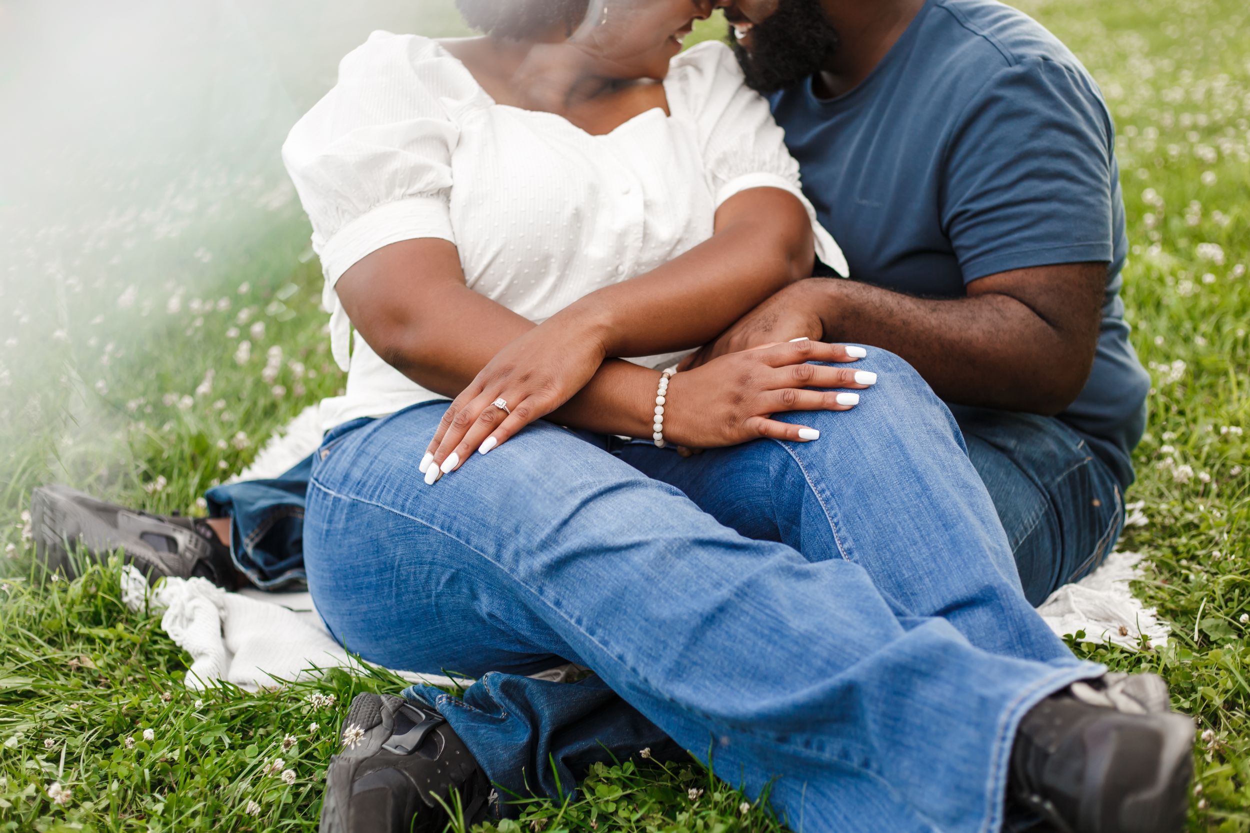 A couple sits together on grass during a romantic outdoor photoshoot.