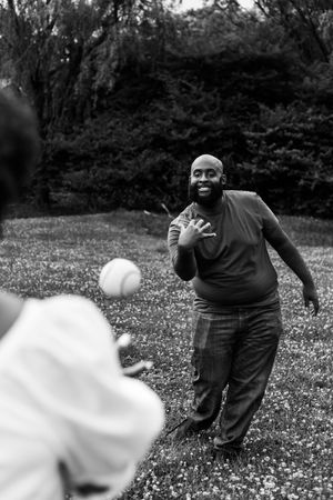 A playful moment captured in black and white as two people toss a ball in a garden setting.