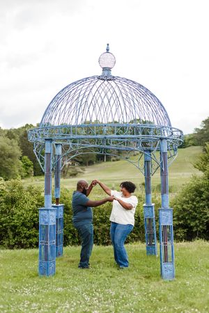 A blue metal gazebo stands in a flowering meadow during a romantic photoshoot.