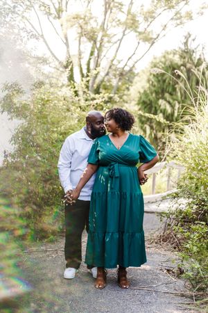 A romantic outdoor photo session showing a couple walking along a wooded path in coordinated green and white outfits.
