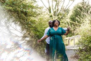 A couple in teal outfits dances together in a misty forest setting during a photo session.