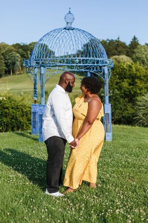 A couple shares an intimate moment in front of a blue garden gazebo on a sunny summer day.