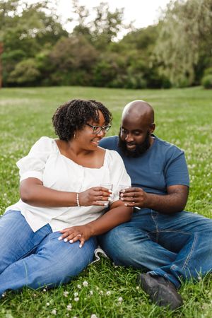 A couple sits together on grass sharing a tender moment while looking at their phones.
