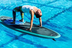 Woman practicing yoga on a paddleboard in a clear blue pool, balancing in a plank pose.