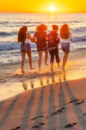 Four girls running into ocean waves at golden sunset on sandy beach.