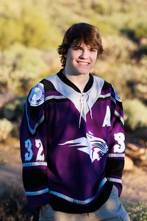 Smiling teen in purple hockey jersey number 32 posing outdoors in desert landscape.