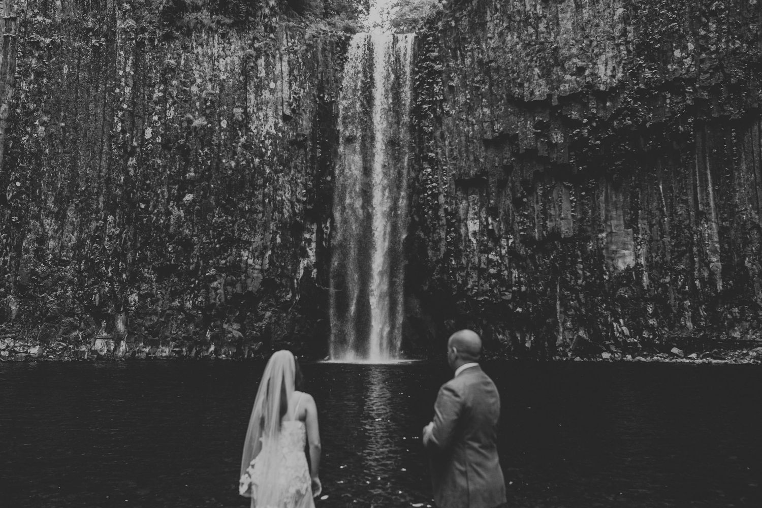 A powerful waterfall cascades down mossy rock formations surrounded by lush green vegetation in a misty forest canyon.