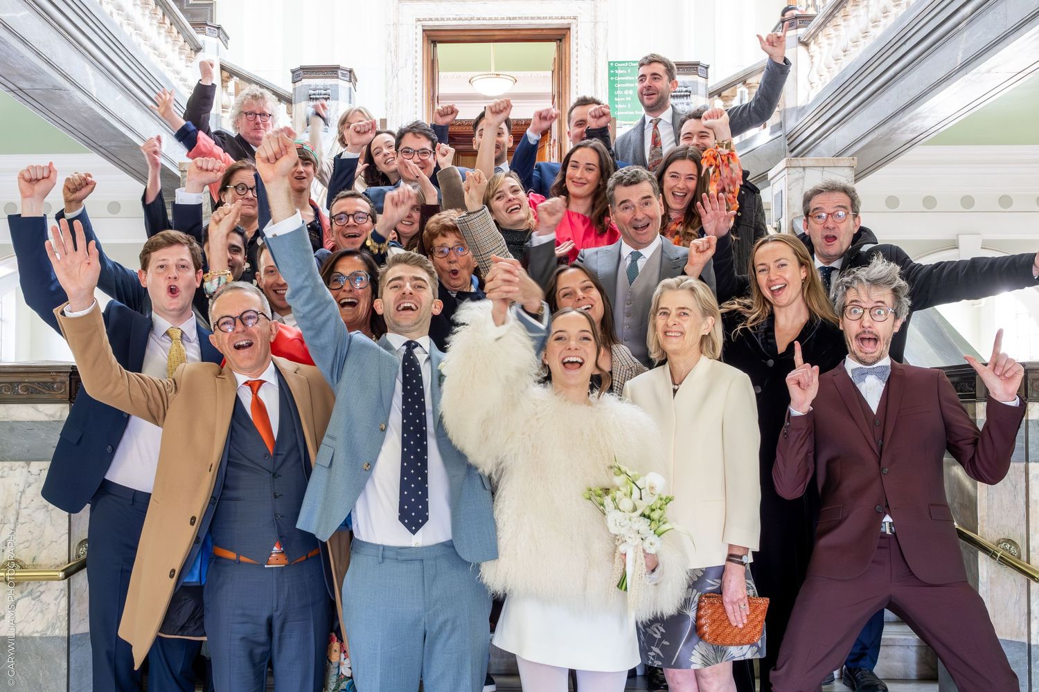 A large group of people, including a bride and groom, posing together outside a building.
