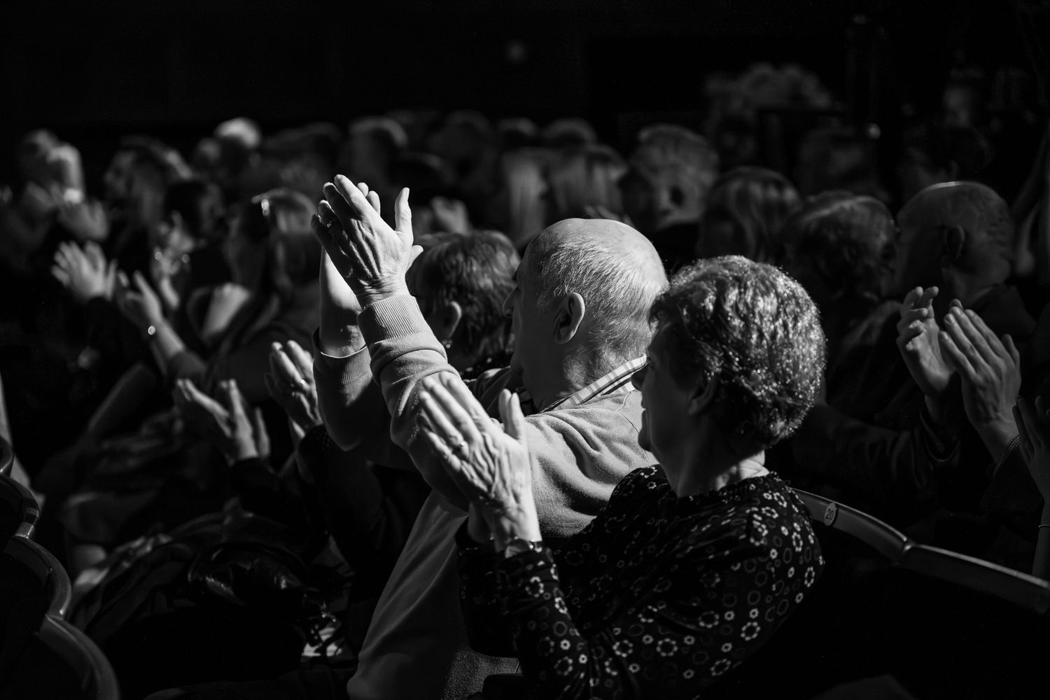 Black and white photo of audience members applauding at a live performance event.