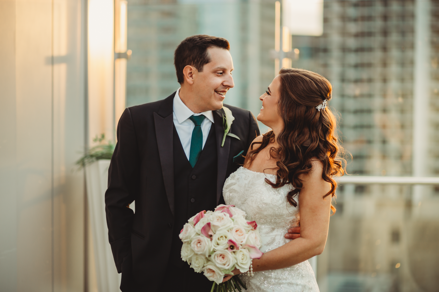 Newlywed couple at their wedding rooftop sunset smiling at each other