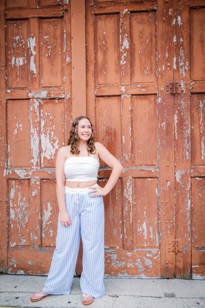 A photo series against rustic orange barn doors shows someone posing in striped pants and a white crop top.