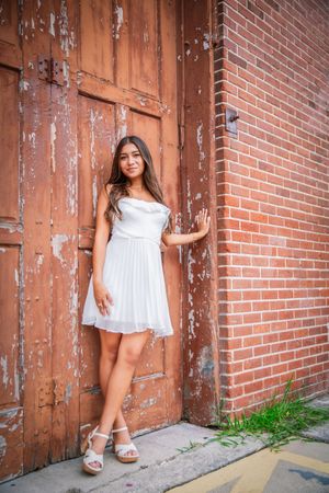 Fashion portraits taken against rustic brick walls and wooden doors showing a flowing white dress.