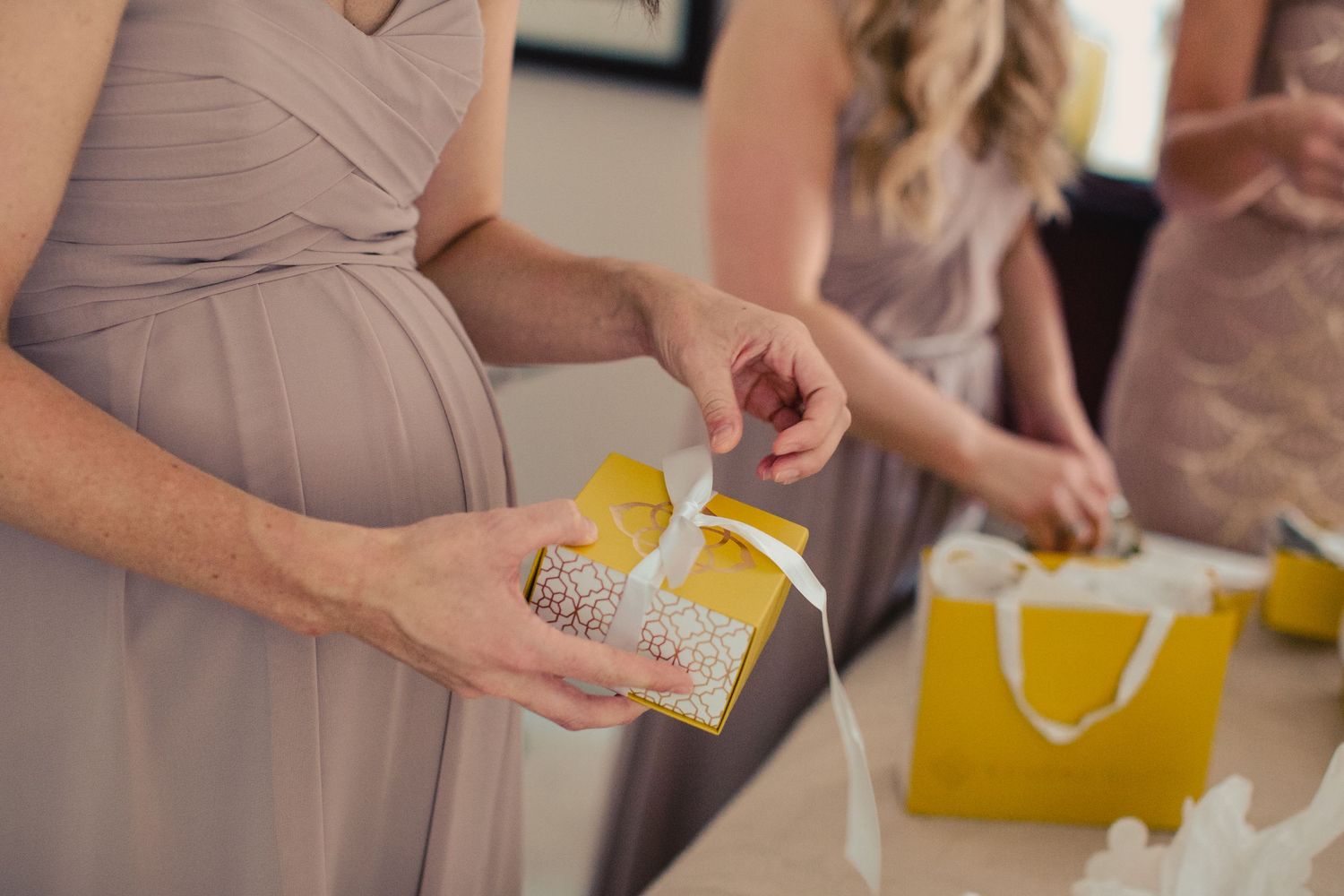 Bridesmaids in taupe dresses opening yellow gift bags and boxes at a bridal shower or wedding celebration.