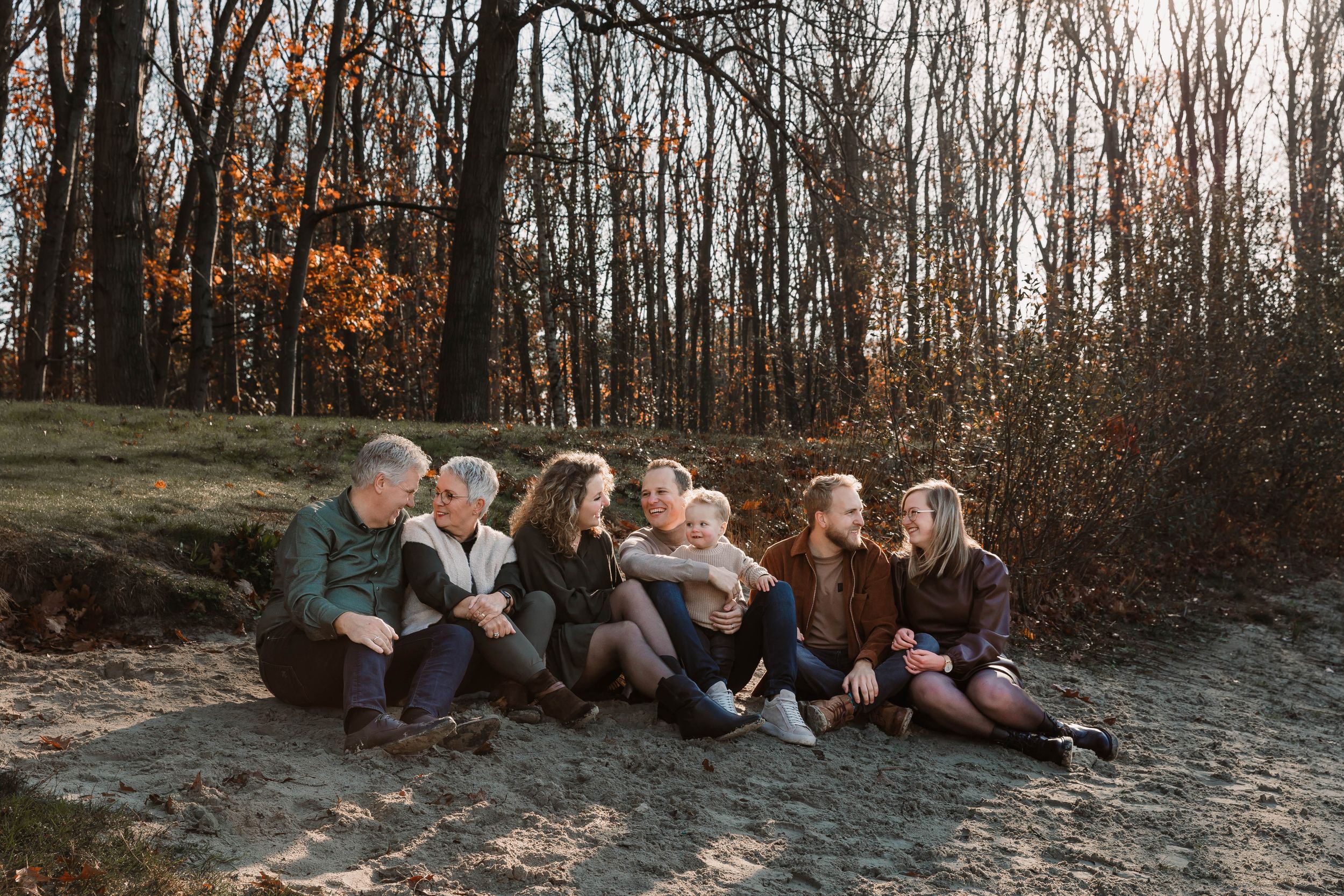 Family photo session in autumn woods with fallen leaves and natural lighting.