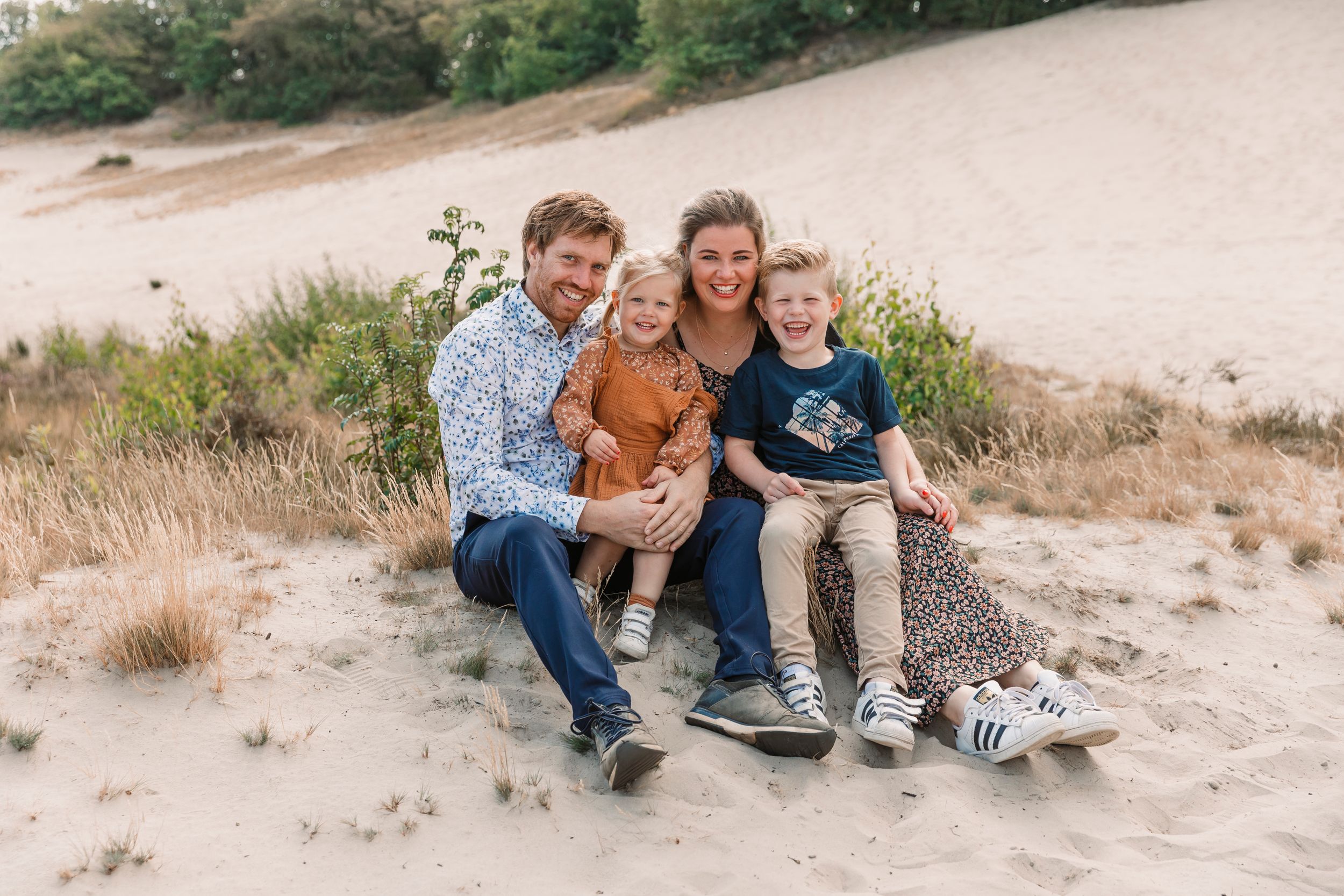 Family portrait session on sandy dunes with natural lighting and casual poses.