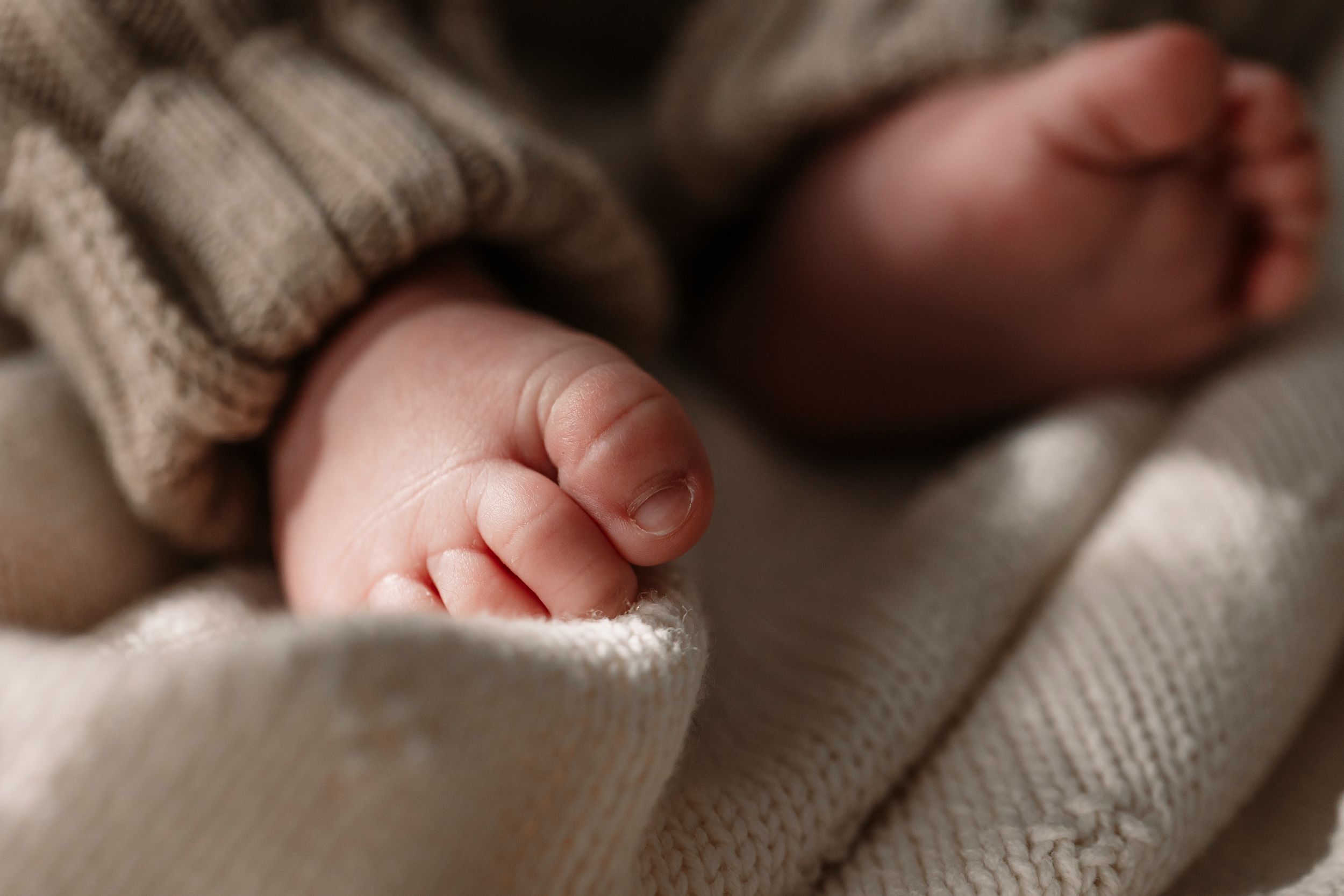 Tender moment of a newborn baby's hand being held on soft white bedding.