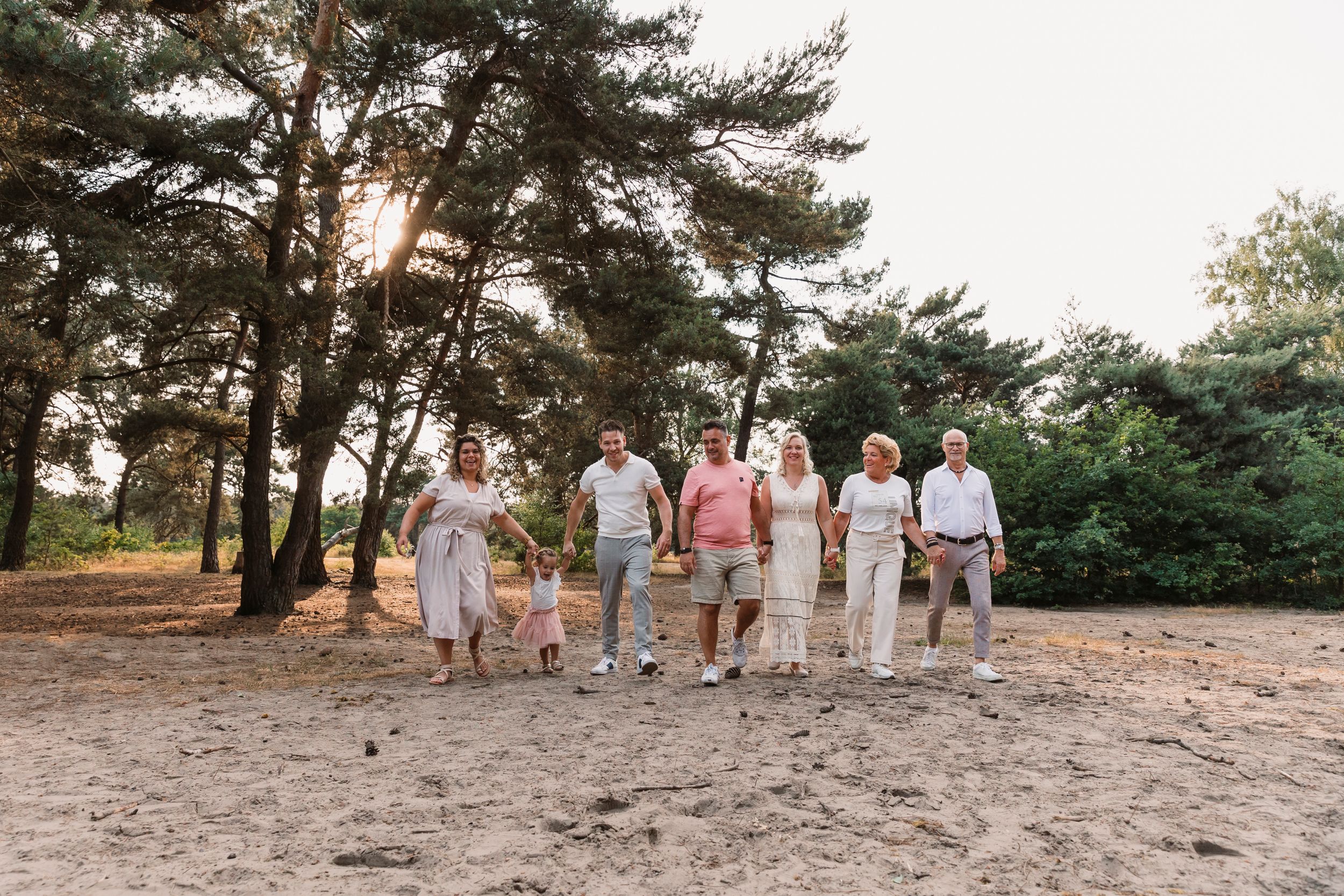 Group walking together along a sandy path through pine trees at sunset.
