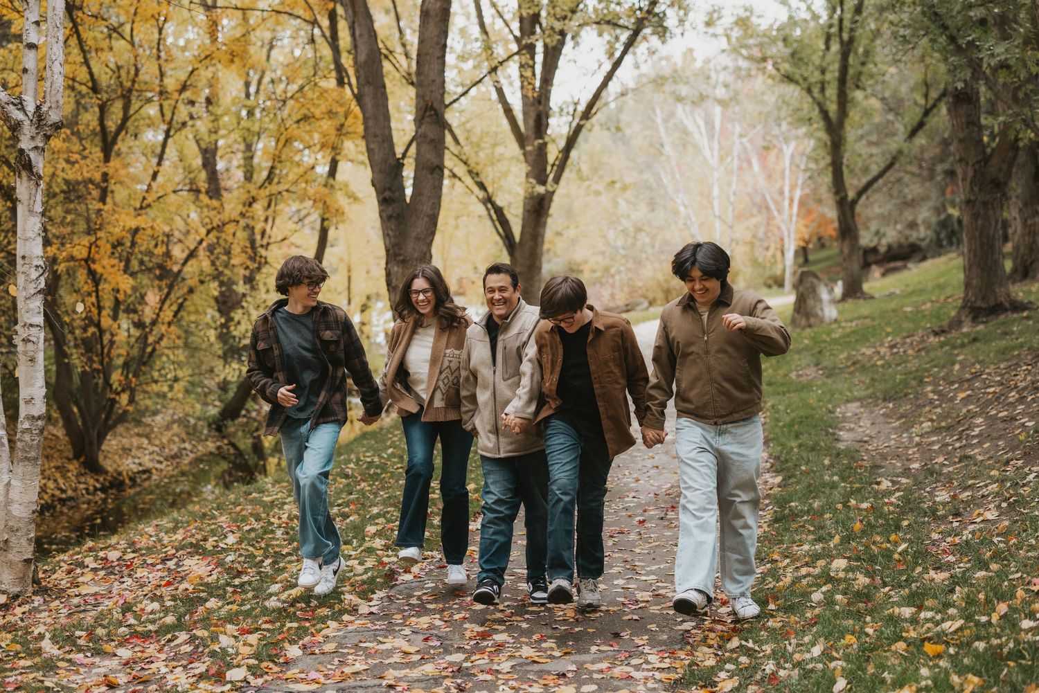 A group walks along a wooded path surrounded by golden autumn foliage and fallen leaves on the ground.