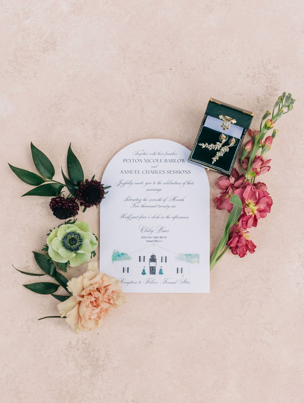 Wedding invitation suite with pink and peach flowers, greenery, and elegant calligraphy laid out on beige background.