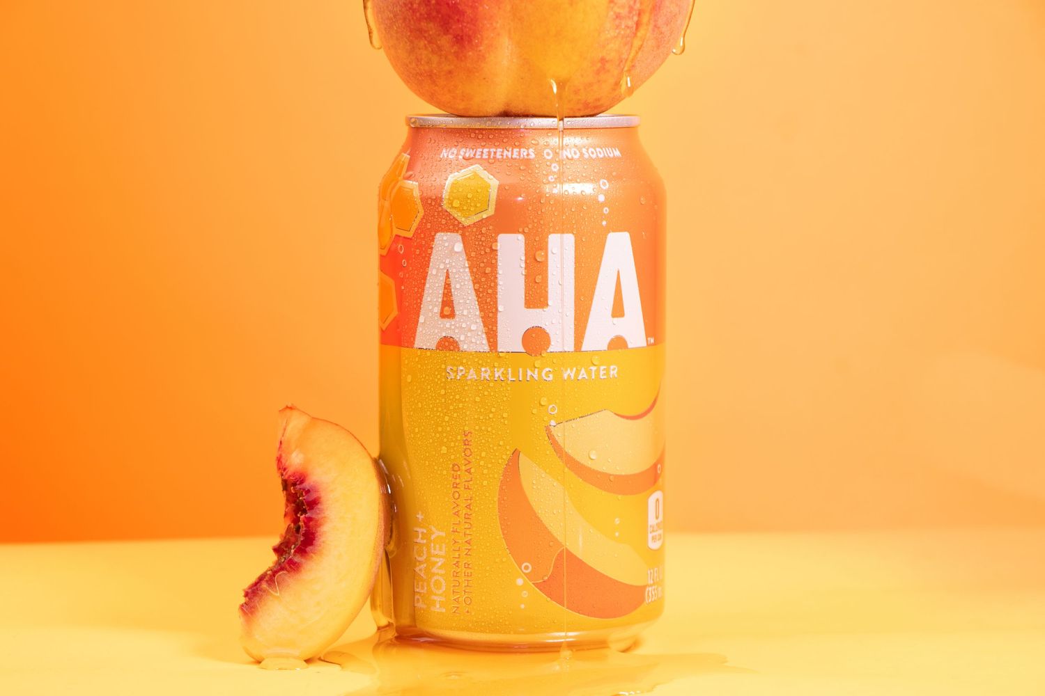 Colorful cans of AHA sparkling water arranged in a row against an orange background with reflective surface.