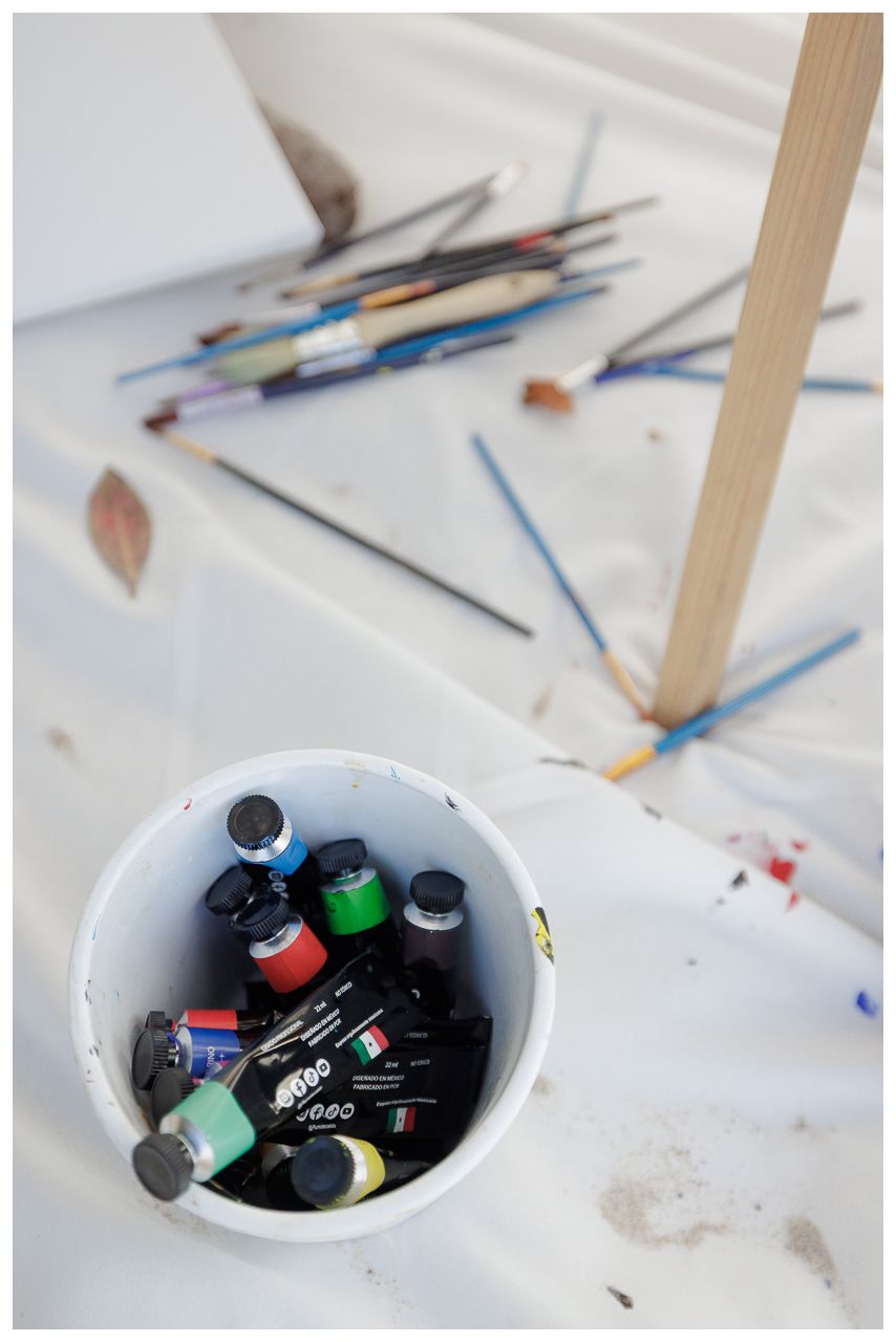 Scattered art supplies and colored pencils on a white surface with a bowl containing markers and art tools.