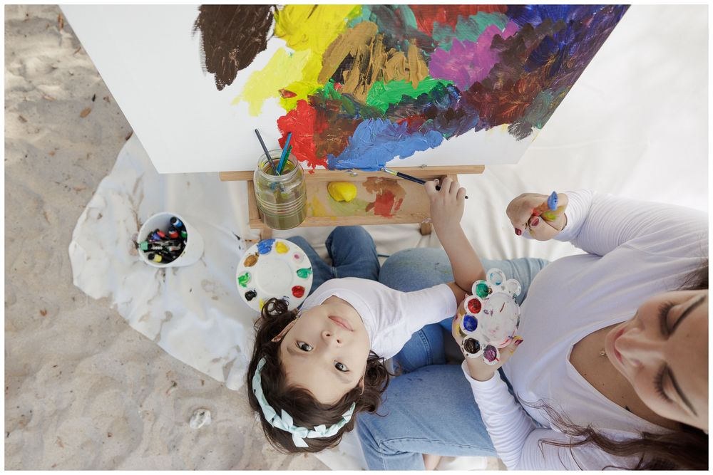 Artists holding colorful paint palettes while working on creative projects in a bright studio space.