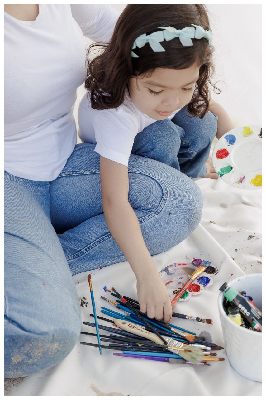 Person in blue jeans sitting on floor with art supplies and colored pencils scattered around.